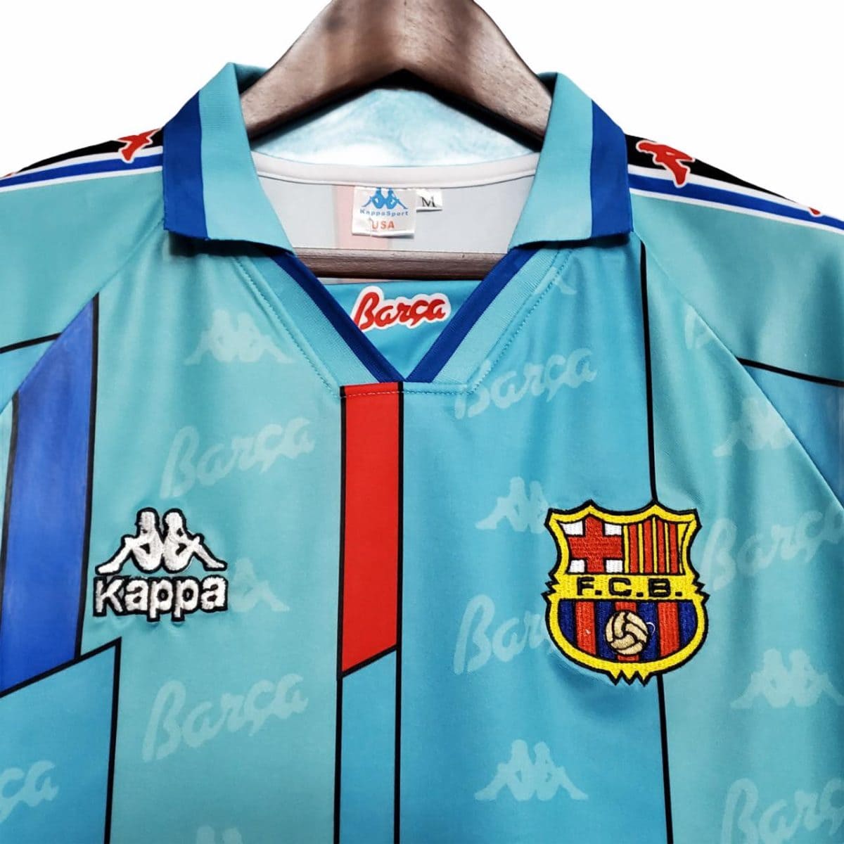 Turquoise FC Barcelona jersey on a hanger, featuring the Kappa logos and the club crest on the chest.