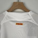 Wooden clothes hanger holding a white bathrobe against a gray wall, with a small yellow-and-red striped label visible at the bottom.