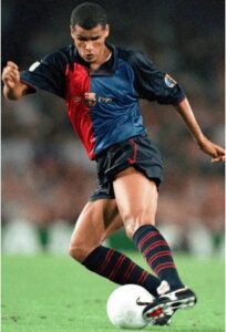 Soccer player in a blue and red jersey kicking a white ball on a grassy field.