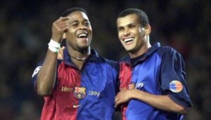 Two male soccer players in blue-and-red Barcelona jerseys laughing with arms around each other.