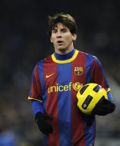 Soccer player in a Barcelona jersey holding a yellow soccer ball on the field.”