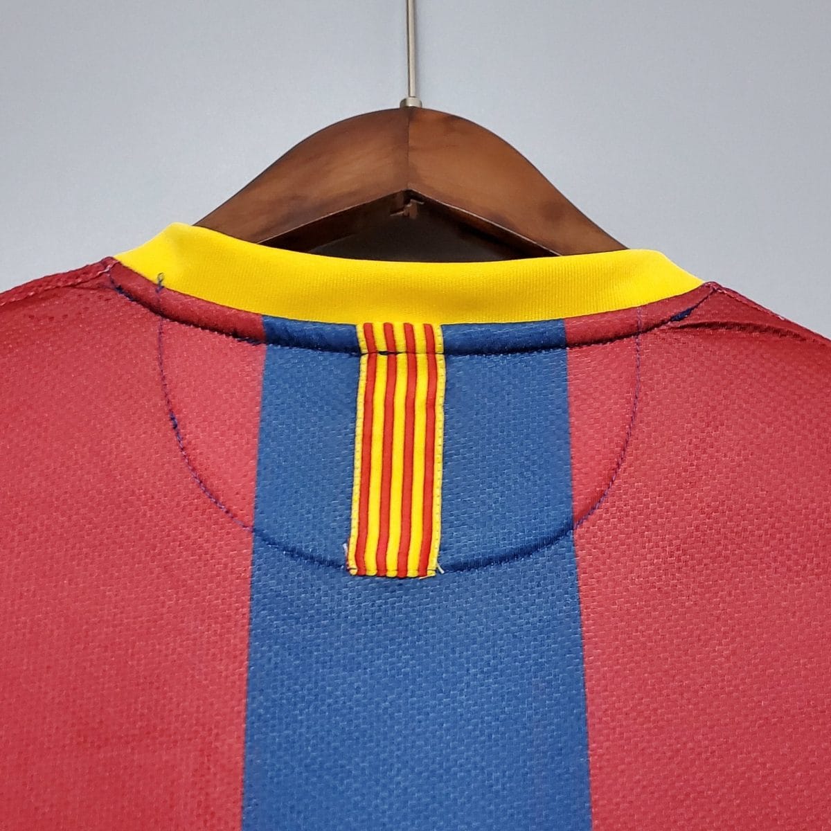 Close-up of a wooden clothes hanger with a red fabric garment featuring blue stripes and a yellow collar against a light background.