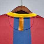 Close-up of a wooden clothes hanger with a red fabric garment featuring blue stripes and a yellow collar against a light background.
