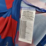 Close-up of a clothing tag on blue and red fabric, listing material and care instructions in multiple languages.