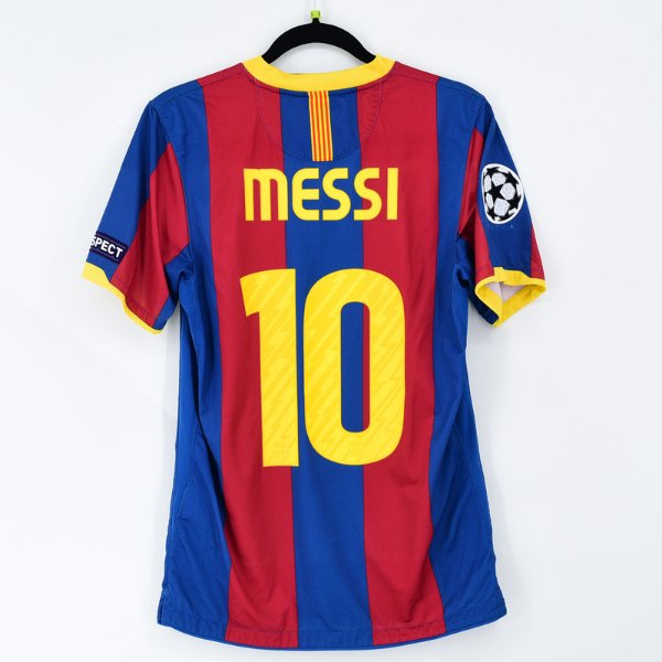 FC Barcelona home soccer jersey with red and blue stripes, 'MESSI' and large yellow 10 on the back, hanging on a hanger (Champions League patch on the left sleeve).