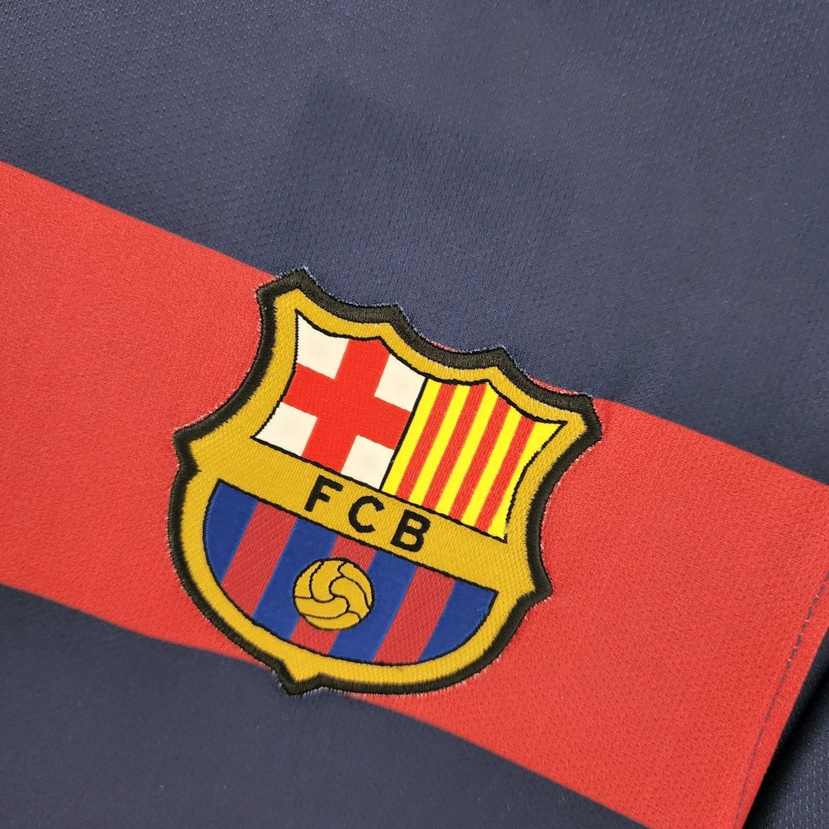 Partial view of the FC Barcelona crest embroidered on blue-and-red fabric, showing part of the shield design.