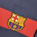 barcelona-classic-201516-final-with-messi-10-badges-jersey-147470 | UAE SPORT STORE Partial view of the FC Barcelona crest embroidered on blue-and-red fabric, showing part of the shield design.