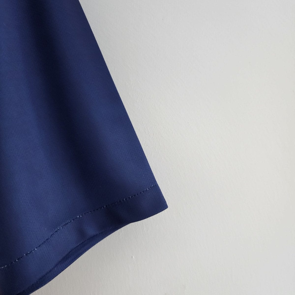 Close-up of blue fabric with visible stitching along the edge against a white background.