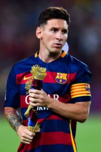 barcelona-classic-201516-final-with-messi-10-badges-jersey-720822 | UAE SPORT STORE Soccer player in Barcelona jersey holding a ceremonial trophy with tassels on the field, wearing a captain's armband