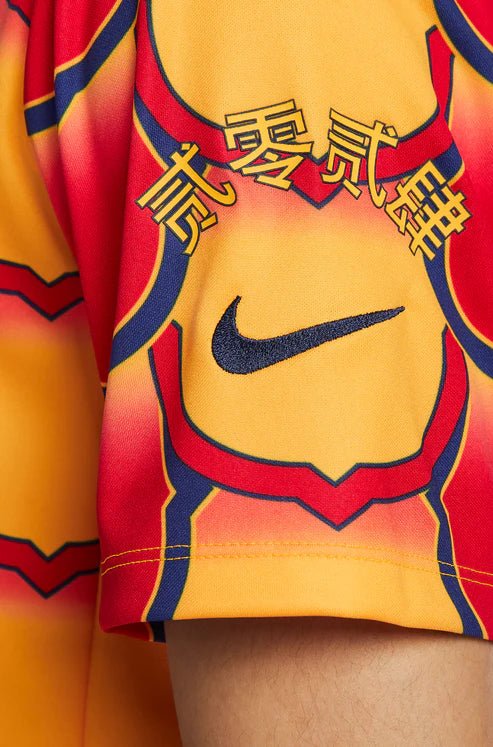 barcelona-gold-pre-match-jersey-2024-404052 | UAE SPORT STORE Close-up of a bright yellow and red sports jersey with a black Nike swoosh and Chinese characters across the chest.