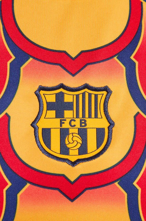 barcelona-gold-pre-match-jersey-2024-656455 | UAE SPORT STORE Close-up of a Barcelona FC crest on a yellow jersey with red and blue trim and bold outlines.