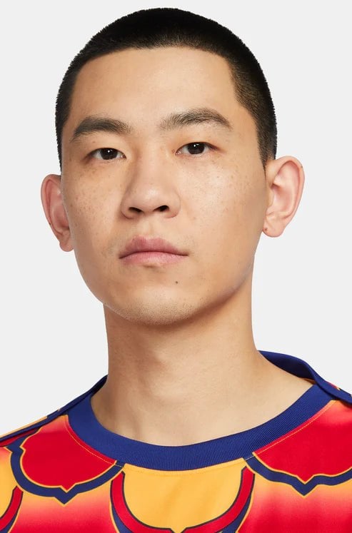 barcelona-gold-pre-match-jersey-2024-671440 | UAE SPORT STORE Close-up portrait of a young Asian man with short hair, neutral expression, wearing a red and yellow patterned shirt against a light background.