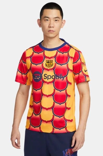 Man wearing a red-and-yellow tile-pattern Barcelona soccer jersey with the Spotify logo, standing against a light gray backdrop.