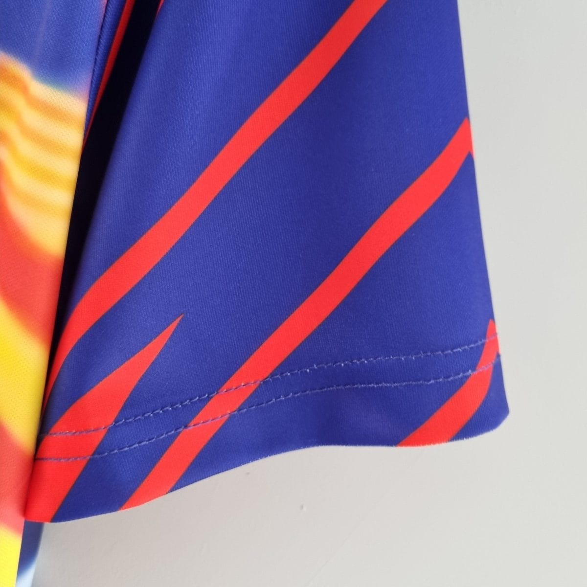Close-up of blue fabric with orange diagonal stripe and a gradient yellow-to-orange area on the left, showing stitching on a garment edge.