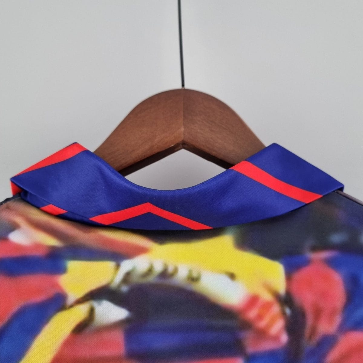 Close-up of a wooden clothes hanger with blue fabric featuring red stripes, against a pale gray background.