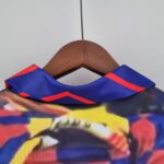 barcelona-home-classic-9394-romario-jersey-814622 | UAE SPORT STORE Close-up of a wooden clothes hanger with blue fabric featuring red stripes, against a pale gray background.