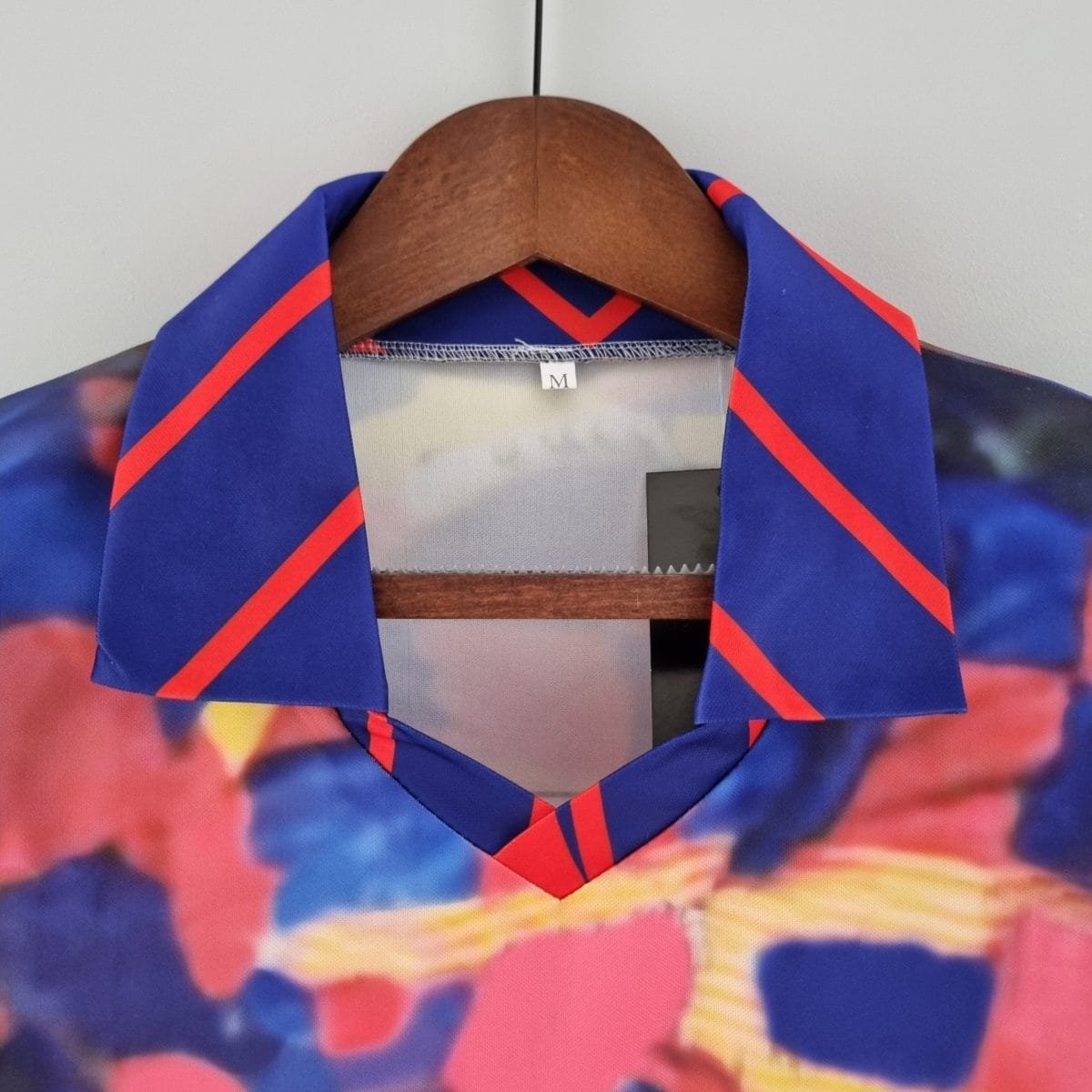 Blue jacket with red diagonal trim on a wooden hanger, size M, hanging against a wall.