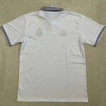 White polo shirt laid flat with a black striped collar and matching black striped sleeve cuffs; faint brand marks visible on the back edge.