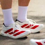 Close-up of white athletic shoes with bold red stripes and white socks on a paved surface.