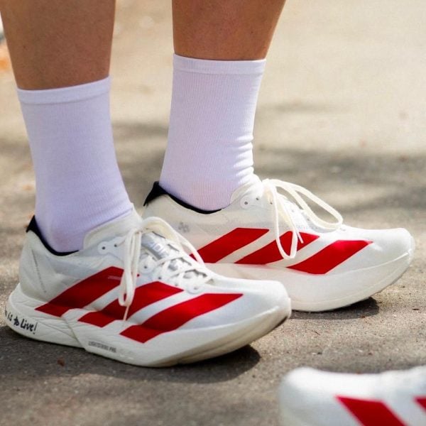 Close-up of white athletic shoes with bold red stripes and white socks on a paved surface.