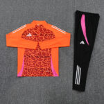 Bright orange leopard-print long-sleeve athletic top with pink side panels, paired with black track pants featuring a pink stripe and white Adidas logo.