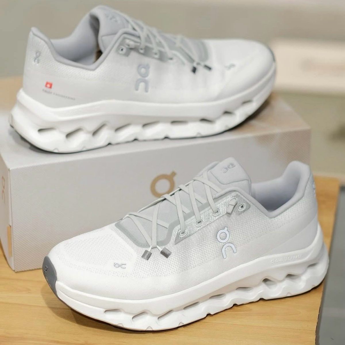 White On running shoes with cloud-like sole on a display box, showcasing light gray details and logo on side, indoors.