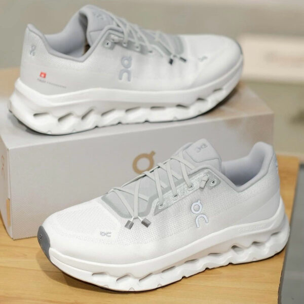 White On running shoes with cloud-like sole on a display box, showcasing light gray details and logo on side, indoors.