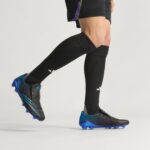 bb98a7ad-f464-49a6-a96f-5ce88474ff95 | UAE SPORT STORE Athlete wearing black knee-high compression socks and blue-black soccer cleats in mid-stride, showing leg muscles.
