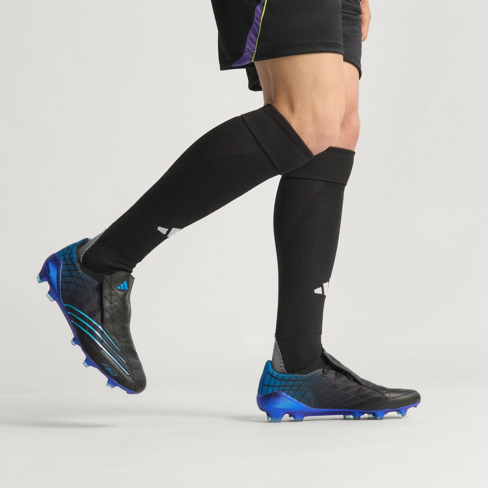 bb98a7ad-f464-49a6-a96f-5ce88474ff95 | UAE SPORT STORE Athlete wearing black knee-high compression socks and blue-black soccer cleats in mid-stride, showing leg muscles.