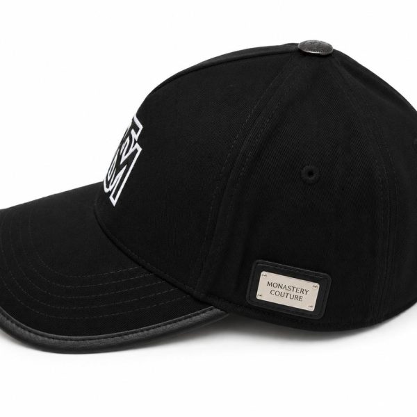 Black baseball cap with a curved brim and a metal 'Monastery Couture' label on the side.