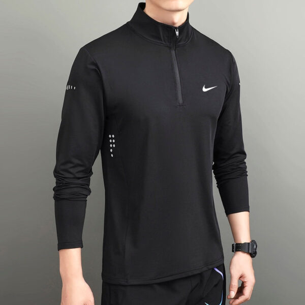 Black Nike long-sleeve quarter-zip athletic top on a man, minimalist design with small white swoosh logo on chest and subtle side dots.