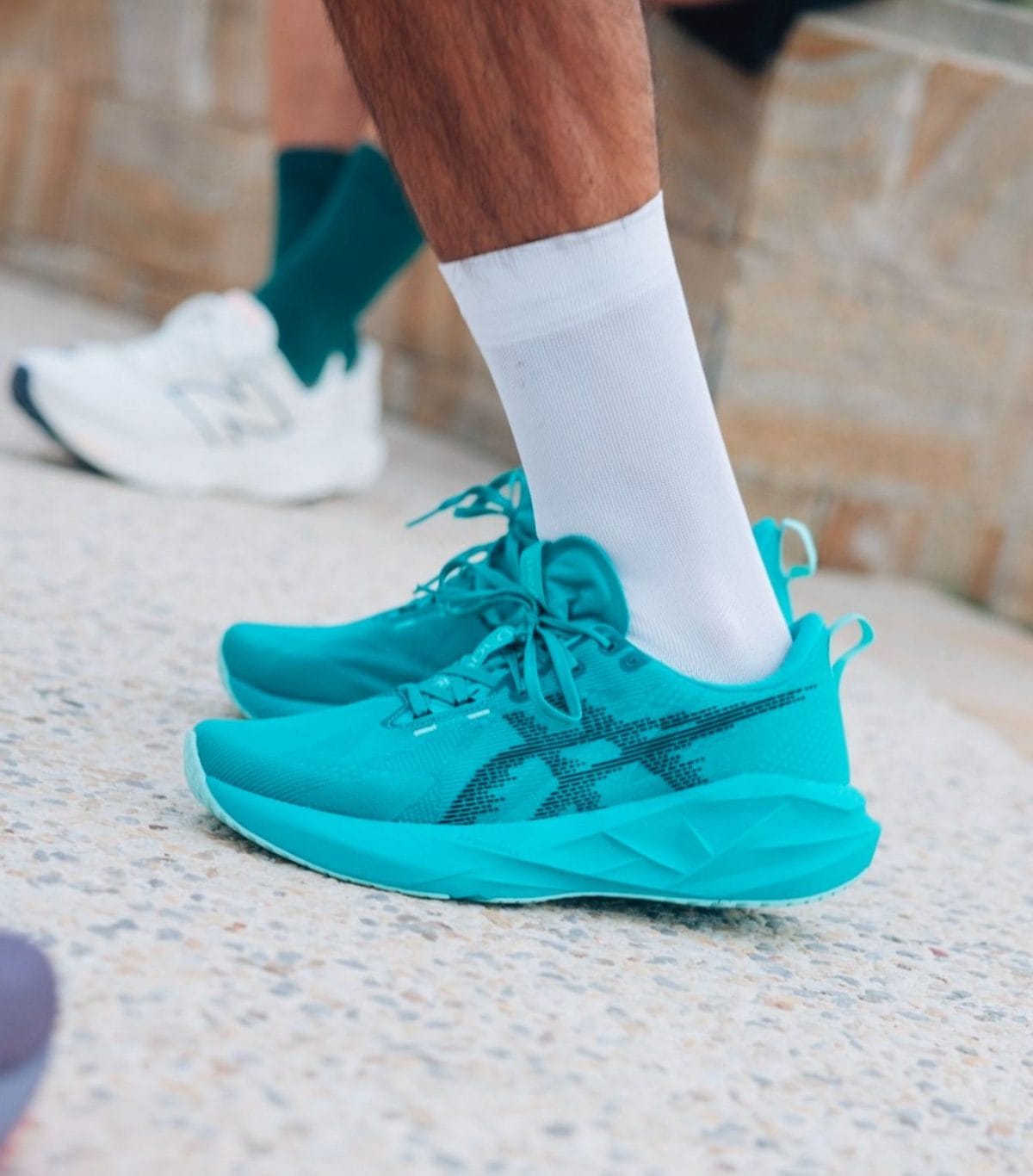 Turquoise running shoes with white socks on a textured outdoor surface.