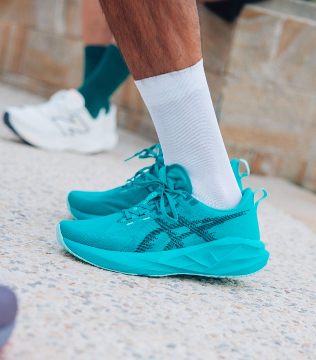 bc2fa7b0-a088-4933-9c4d-44e34433fd45 | UAE SPORT STORE Turquoise running shoes with white socks on a textured outdoor surface.
