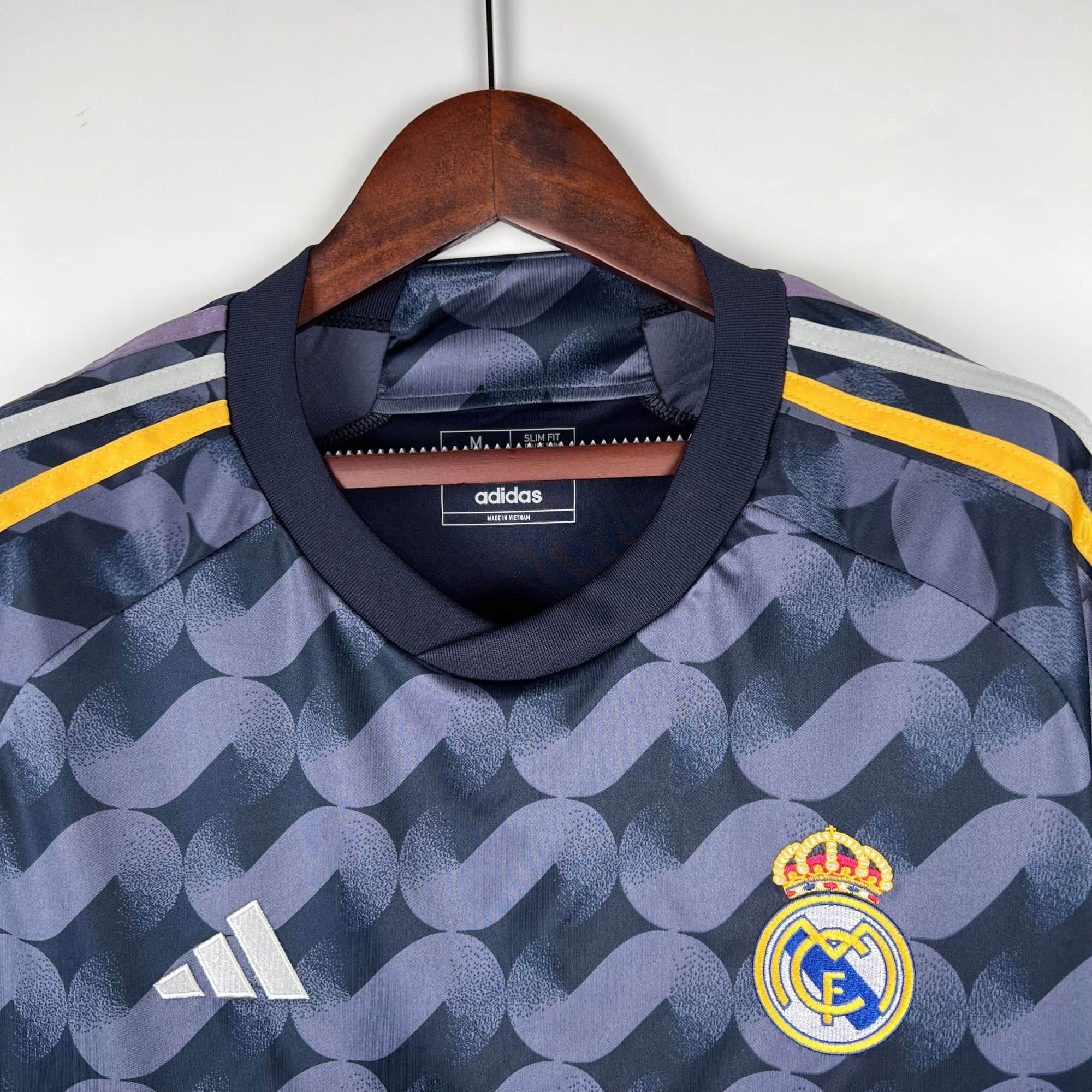 bc76033d | UAE SPORT STORE Real Madrid football jersey on a wooden hanger, navy blue with yellow stripes and the Real Madrid crest visible.