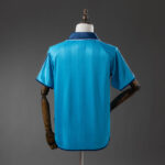 bcd2b36a | UAE SPORT STORE Back view of a bright blue polo jersey on a dress form with a navy collar and white trim along the edge.