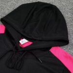 Black hoodie with pink accents on the sleeves, laid flat with hood up and drawstrings hanging.