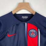 Navy PSG football jersey on a wooden hanger with a round Paris Saint-Germain badge visible on the chest area