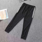 Black athletic jogger pants with elastic waist and white side stripes laid on a gray carpet.