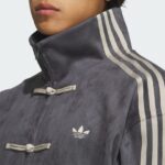 Close-up of a person wearing a dark blue Adidas jacket with a high collar, white stripes along the sleeves, and a trefoil logo on the chest.
