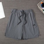 Grey athletic shorts with a black drawstring, elastic waistband, and an Adidas logo on the left thigh area, laid flat on a wooden surface.