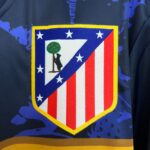Decorative shield-shaped patch on dark fabric: blue field with white stars, red and white stripes, a diagonal blue stripe, green tree emblem, yellow border.
