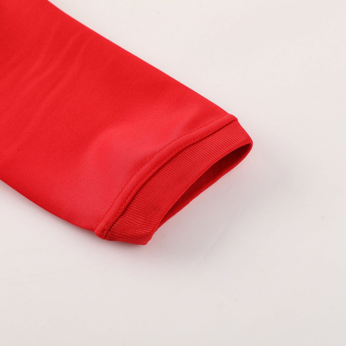 Close-up of red fabric with a folded edge and visible stitching against a pale background.