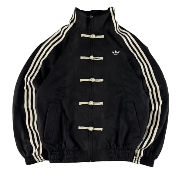 Black Adidas track jacket with cream toggle closures and three white stripes down the sleeves; small Adidas logo on the left chest.