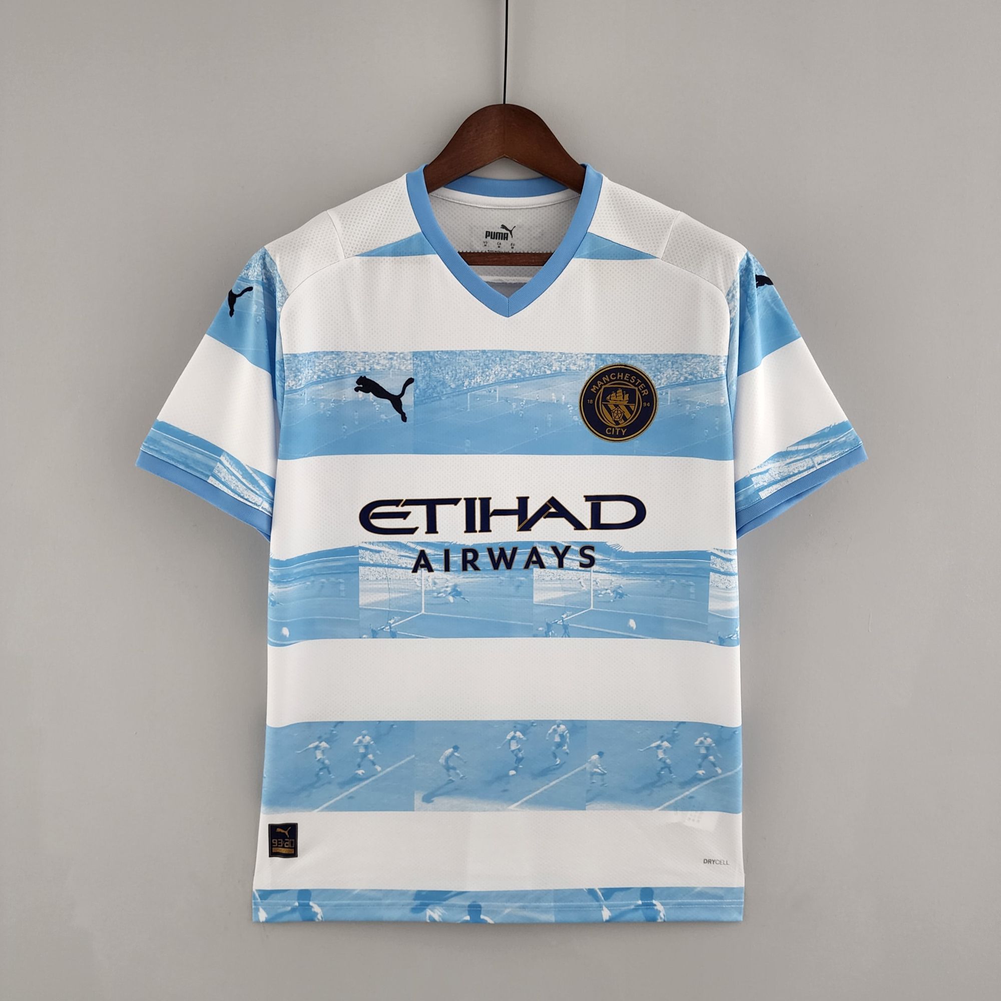be9044c4_db13635d-1baa-4b5c-949c-fe2fe10e5bc0 | UAE SPORT STORE Manchester City home football jersey on a wooden hanger, sky-blue and white stripes with Etihad Airways sponsor visible on the chest badge and sponsor.