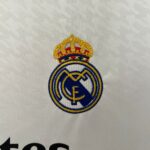 Partial embroidered crest featuring a gold crown above blue and white elements on white fabric, top portion visible