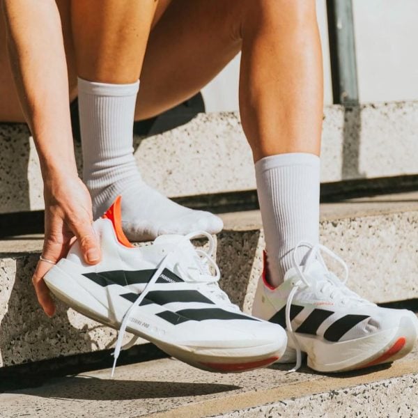 Person on concrete steps tying white athletic sneakers with black stripes and white socks.