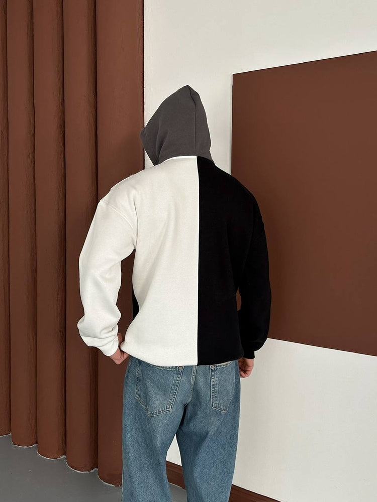 bedogiyimm_247b0aeb8dfb262afca479eb0e9a06e5 | UAE SPORT STORE Back view of a person wearing a two-tone color-block hoodie (white left panel, black right panel) with a gray hood, paired with blue jeans, standing in a room with brown panels on the wall.