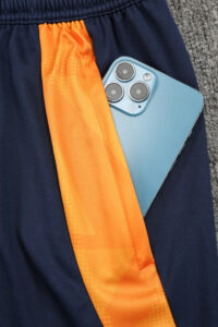 Blue athletic shorts with an orange vertical stripe and a light-blue smartphone tucked into the pocket at the front.
