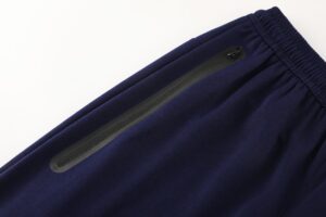 Close-up of dark blue fabric with a black zipper running along the edge and an elastic waistband at the top corner, suggesting athletic pants.