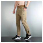 Male model wearing tan athletic joggers with an elastic waistband and zippered ankle cuffs, paired with black Nike sneakers.